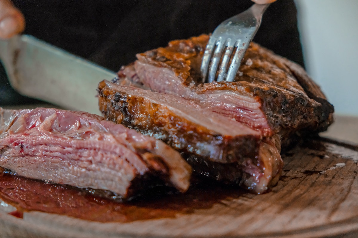 Grilled asado beef being sliced on a wooden board, Argentine parrilla
