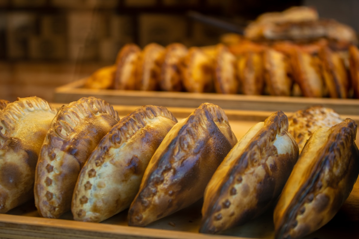 Freshly baked Argentine empanadas with crimped edges on a wooden board